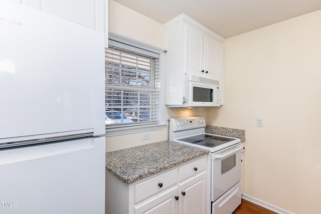 kitchen with a textured ceiling, light stone counters, white appliances, and white cabinetry