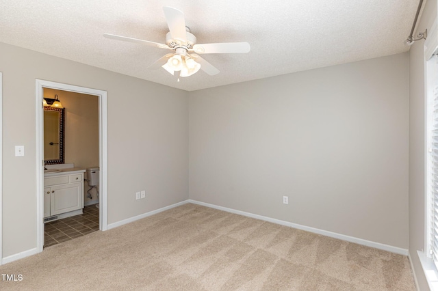 unfurnished bedroom featuring light colored carpet, ceiling fan, a textured ceiling, ensuite bath, and baseboards