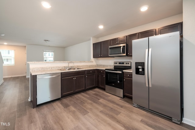 kitchen with stainless steel appliances, a sink, dark brown cabinetry, wood finished floors, and a peninsula