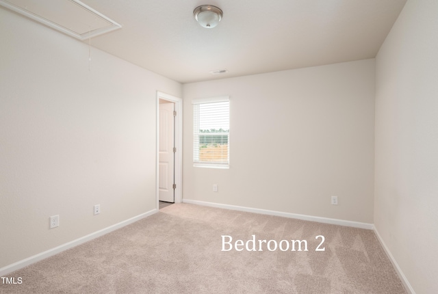 carpeted empty room with attic access and baseboards