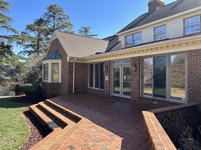 back of property featuring brick siding, a shingled roof, a chimney, and a patio