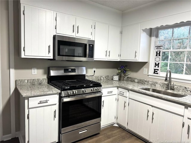 kitchen with stainless steel appliances, dark wood-style flooring, a sink, white cabinets, and light stone countertops