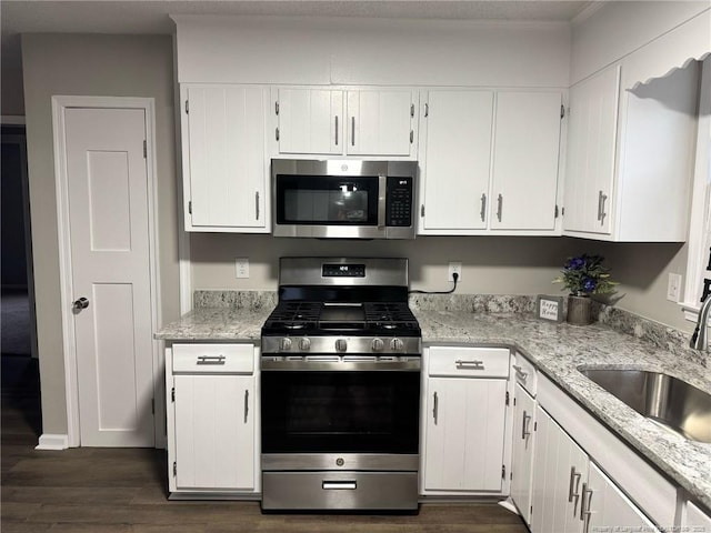 kitchen with dark wood finished floors, stainless steel appliances, white cabinetry, a sink, and light stone countertops