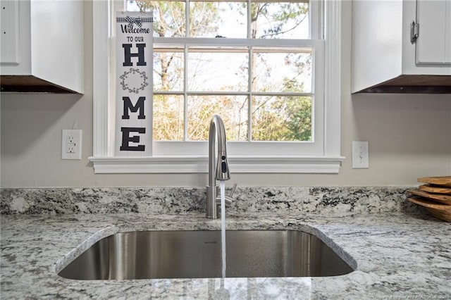 interior details featuring light stone counters, white cabinetry, and a sink