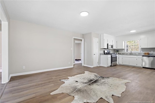 kitchen featuring a sink, white cabinets, light wood-style floors, baseboards, and appliances with stainless steel finishes