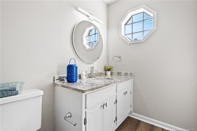 bathroom with toilet, vanity, baseboards, and wood finished floors