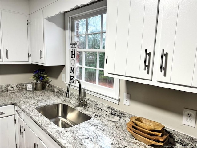 kitchen featuring light stone counters, white cabinetry, and a sink