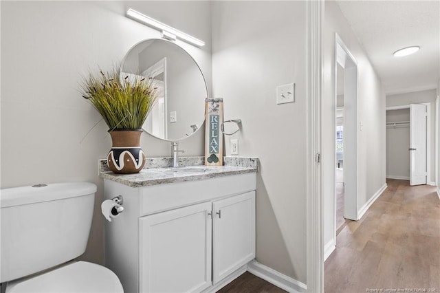 half bathroom with baseboards, vanity, toilet, and wood finished floors