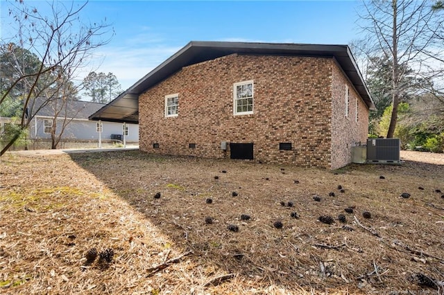 view of side of home with central AC, brick siding, and crawl space