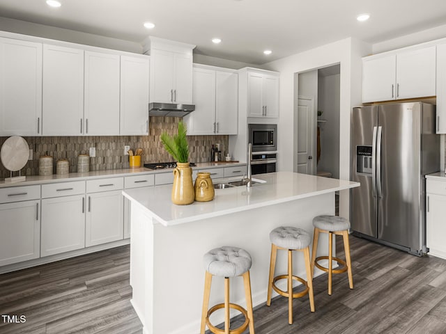 kitchen featuring appliances with stainless steel finishes, a kitchen island with sink, light countertops, under cabinet range hood, and white cabinetry