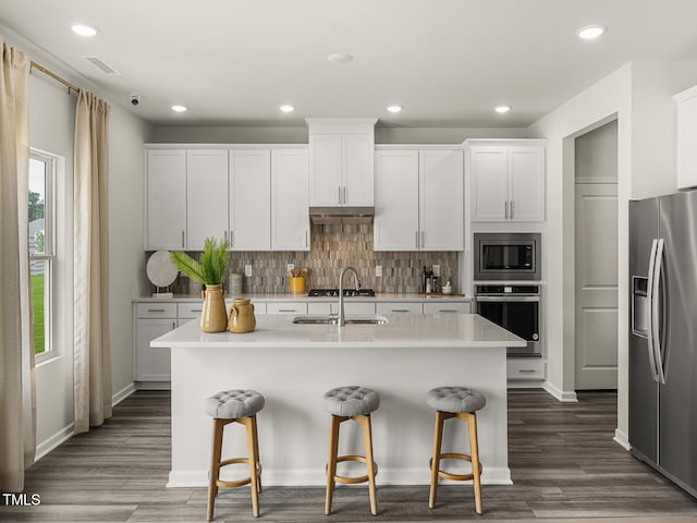 kitchen with white cabinetry, a kitchen island with sink, appliances with stainless steel finishes, and light countertops