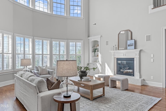 living room featuring baseboards, a glass covered fireplace, wood finished floors, and a healthy amount of sunlight