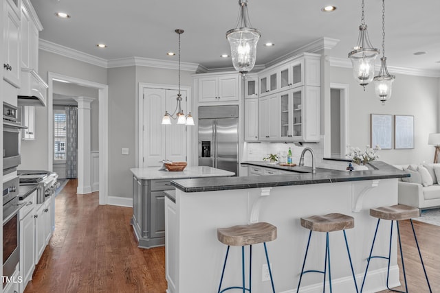 kitchen with dark wood-style flooring, decorative backsplash, appliances with stainless steel finishes, glass insert cabinets, and ornamental molding