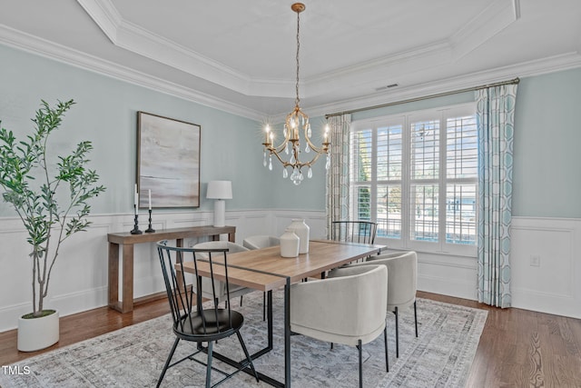 dining area with a tray ceiling, wainscoting, and wood finished floors