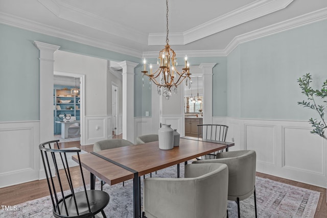 dining room with a chandelier, wood finished floors, a raised ceiling, and decorative columns