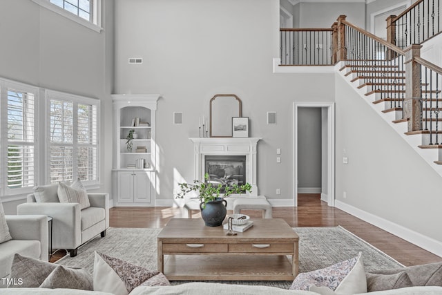 living room featuring wood finished floors, a high end fireplace, visible vents, baseboards, and stairway