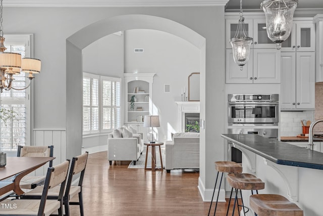 kitchen with a chandelier, wood finished floors, dark countertops, and arched walkways