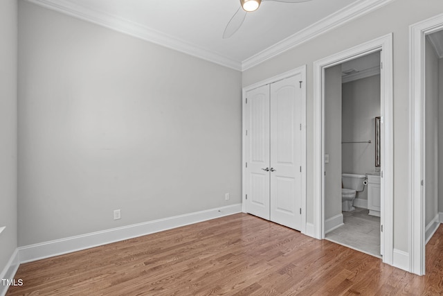 unfurnished bedroom featuring baseboards, ensuite bath, ornamental molding, wood finished floors, and a closet