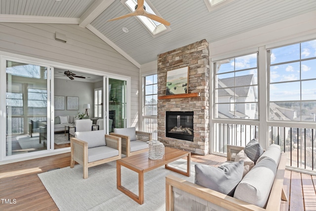 sunroom featuring lofted ceiling with skylight, ceiling fan, and a stone fireplace