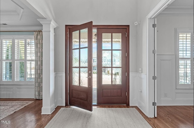 foyer entrance with a decorative wall, wood finished floors, ornamental molding, wainscoting, and ornate columns