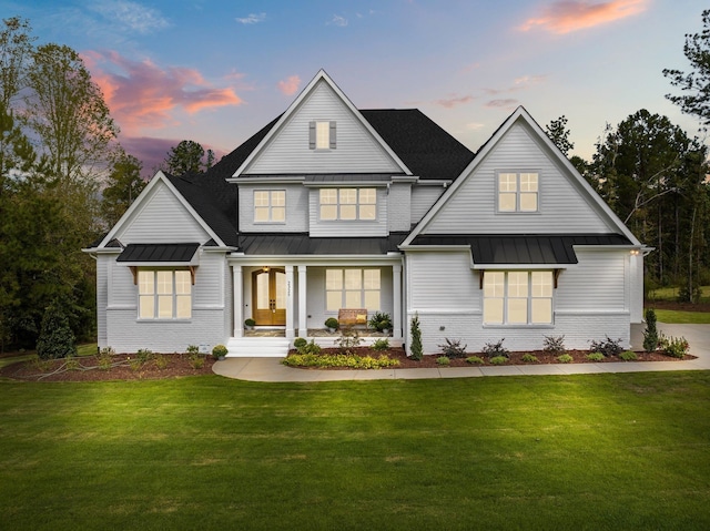 view of front of home with a porch, a standing seam roof, a front lawn, and brick siding