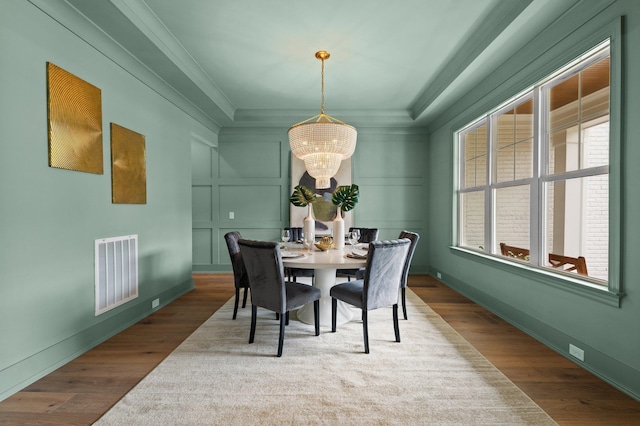 dining room featuring a decorative wall, a notable chandelier, wood finished floors, visible vents, and crown molding