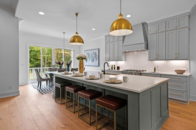 kitchen featuring an island with sink, a kitchen breakfast bar, custom exhaust hood, gray cabinets, and a sink