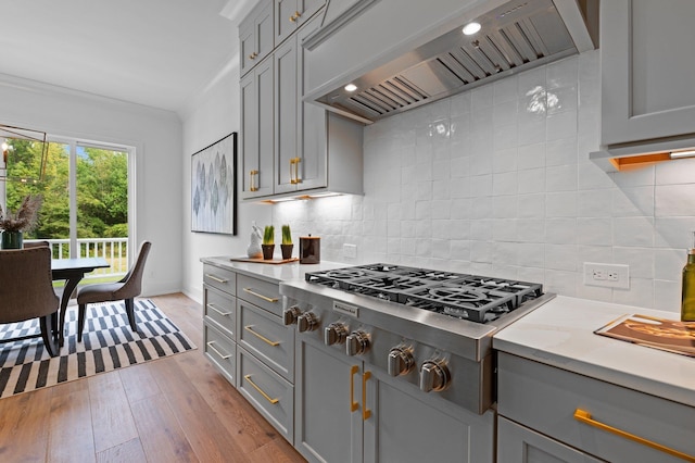 kitchen featuring wall chimney range hood, light wood-type flooring, backsplash, gray cabinets, and stainless steel gas stovetop