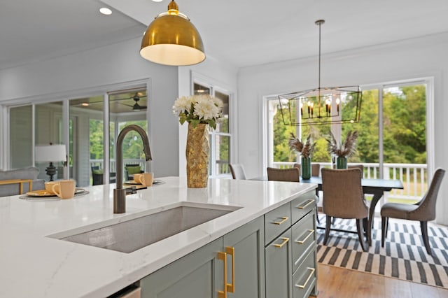 kitchen featuring light wood finished floors, light stone counters, gray cabinets, pendant lighting, and a sink