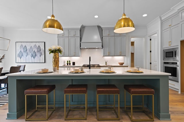 kitchen with a kitchen breakfast bar, light countertops, appliances with stainless steel finishes, gray cabinets, and custom exhaust hood