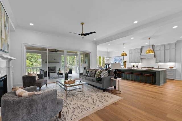 living area with light wood-style floors, ceiling fan, crown molding, and a glass covered fireplace