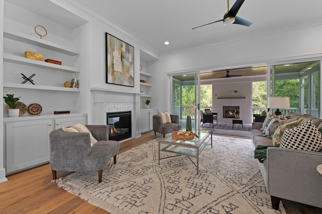 living room with ceiling fan, a healthy amount of sunlight, light wood-style floors, a glass covered fireplace, and crown molding