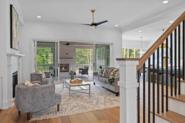 living area featuring light wood-style floors, recessed lighting, a fireplace, and ceiling fan with notable chandelier