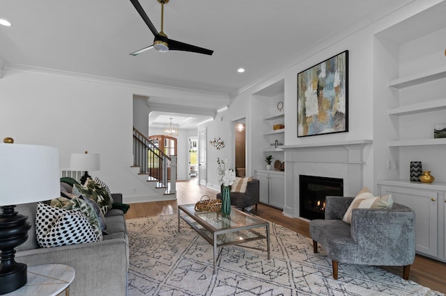 living area with built in shelves, a warm lit fireplace, ornamental molding, and stairway