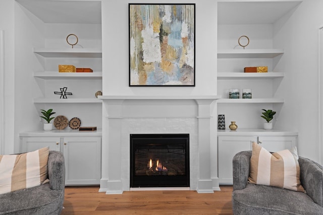 living area with light wood-style flooring, a fireplace, and built in features