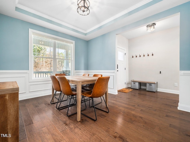 dining room featuring an inviting chandelier, a raised ceiling, dark wood finished floors, and wainscoting