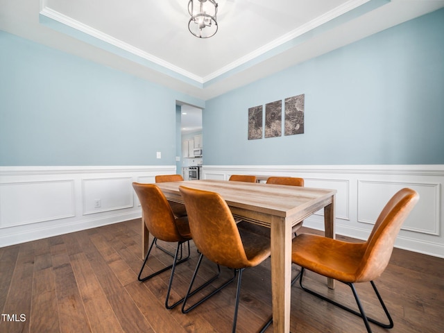 dining area with ornamental molding, wainscoting, a tray ceiling, dark wood finished floors, and an inviting chandelier