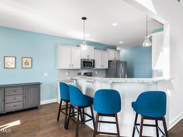 kitchen with white cabinets, a kitchen breakfast bar, dark wood-style flooring, stainless steel appliances, and pendant lighting