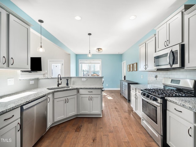 kitchen with decorative backsplash, appliances with stainless steel finishes, hanging light fixtures, light stone countertops, and a sink