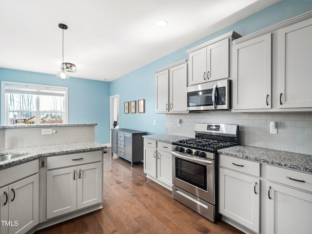 kitchen with pendant lighting, appliances with stainless steel finishes, dark wood-type flooring, white cabinetry, and light stone countertops