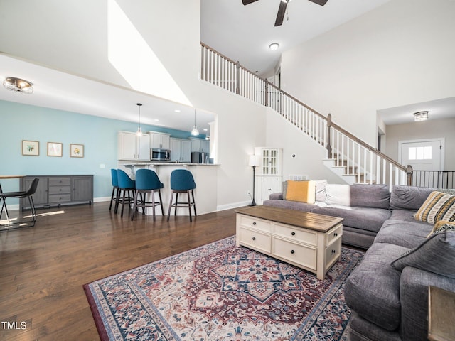 living area with a towering ceiling, dark wood-style floors, and baseboards