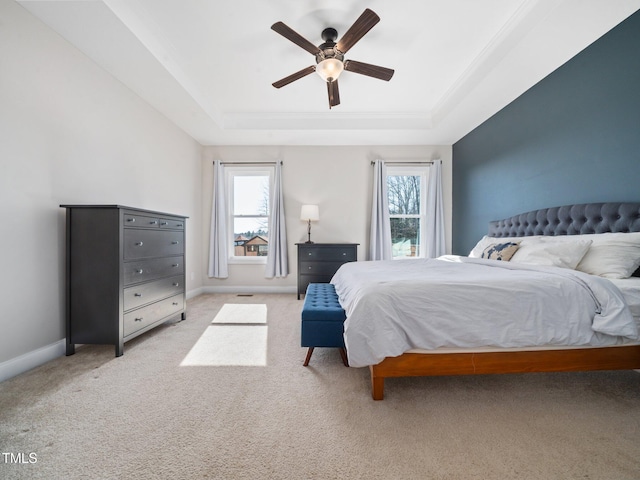 bedroom with multiple windows, a raised ceiling, and light colored carpet