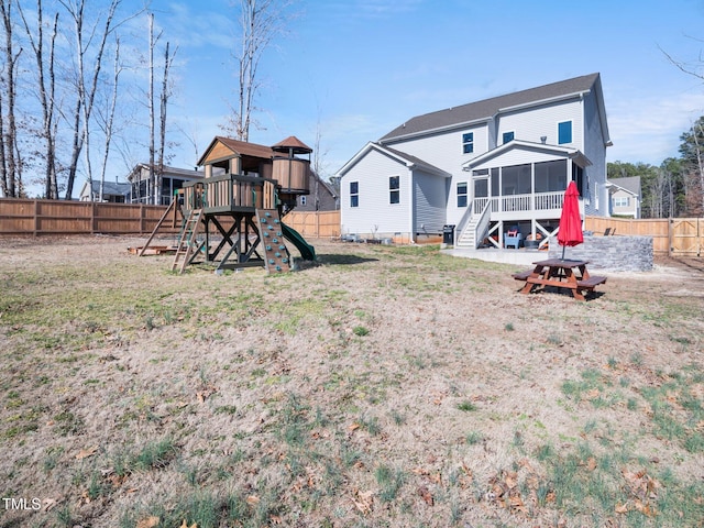 back of property with a sunroom, a fenced backyard, and a playground