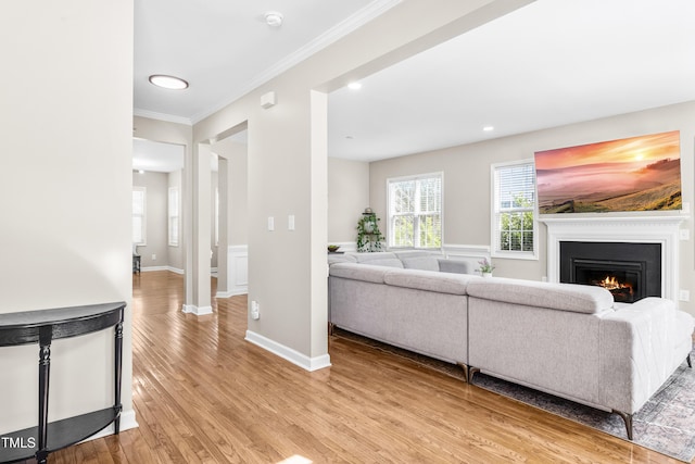 living room with recessed lighting, baseboards, a lit fireplace, light wood-type flooring, and crown molding