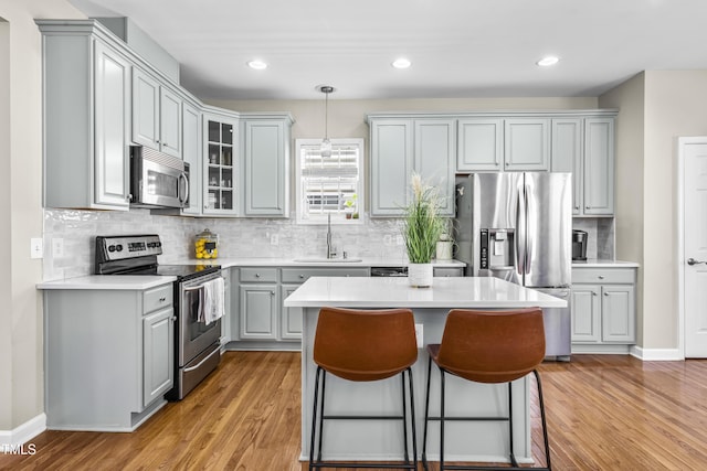 kitchen with stainless steel appliances, a sink, light countertops, gray cabinets, and glass insert cabinets