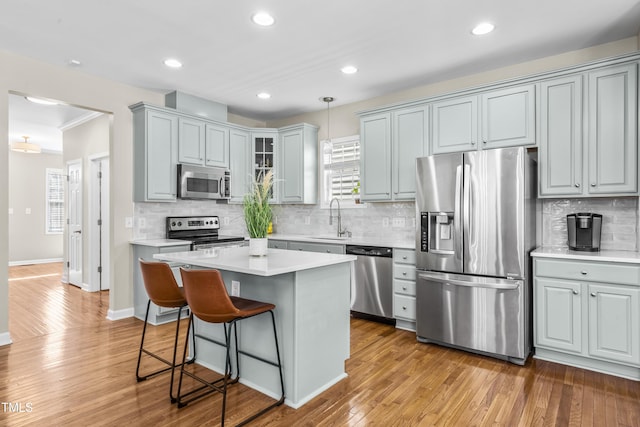 kitchen with glass insert cabinets, appliances with stainless steel finishes, decorative light fixtures, light countertops, and a sink