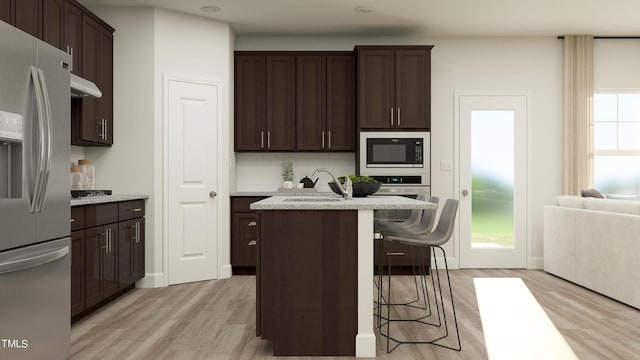 kitchen featuring stainless steel fridge, a center island with sink, a breakfast bar area, built in microwave, and a sink