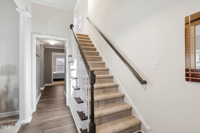 stairway with baseboards, crown molding, ornate columns, and wood finished floors