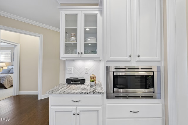 kitchen featuring white cabinets, tasteful backsplash, stainless steel microwave, glass insert cabinets, and crown molding