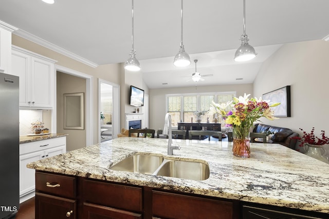 kitchen featuring stainless steel refrigerator, open floor plan, decorative light fixtures, a fireplace, and a sink